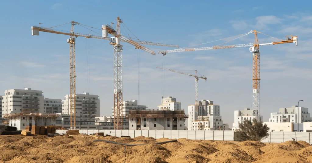 בניין מגורים רב קומות בשלבי בנייה מתקדמים עם מנופים על רקע שמיים כחולים.
